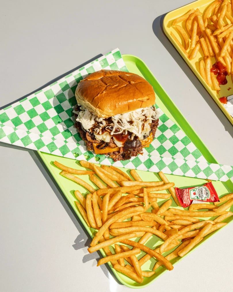 A burger with cheese, onions, and sauce on a green checkered wrapper, with fries and ketchup.